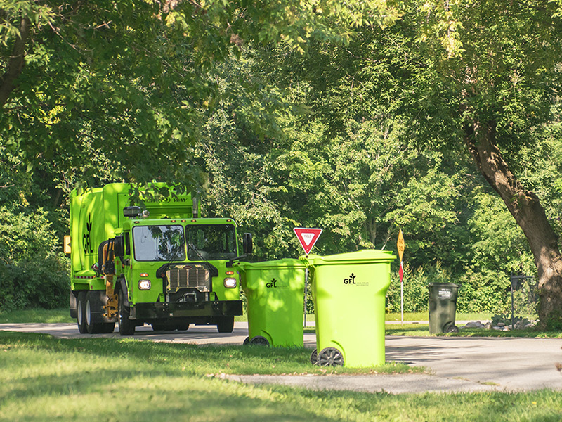A GFL collection truck picks up trash in a neighborhood.