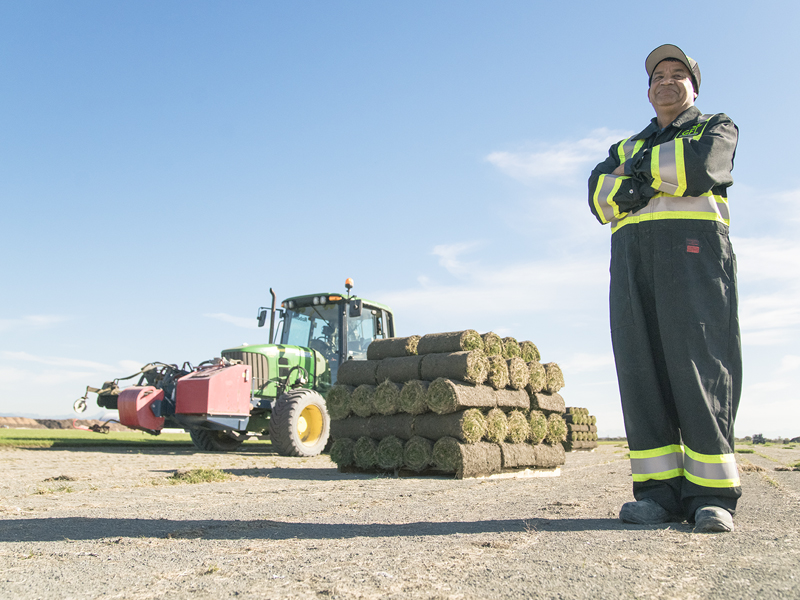A GFL employee smiles confidently arms crossed as a tractor sits behind him
