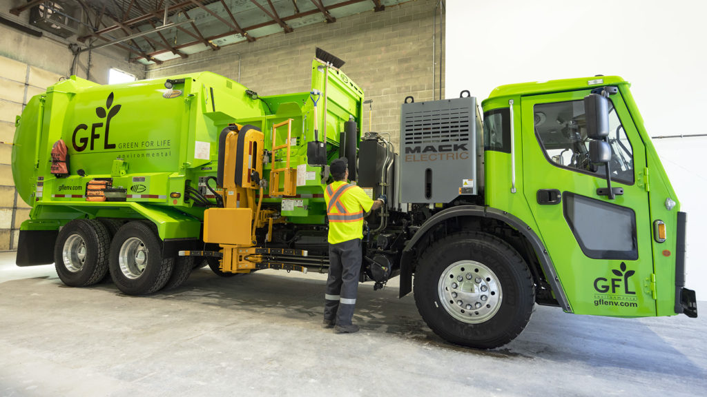 Man in a high-vis vest standing in front of GFL's new signature green electric truck in its garage. 